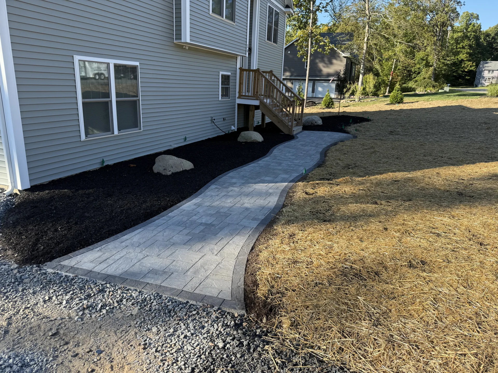 Paver walkway with fresh mulch beds and decorative boulders at a new construction home